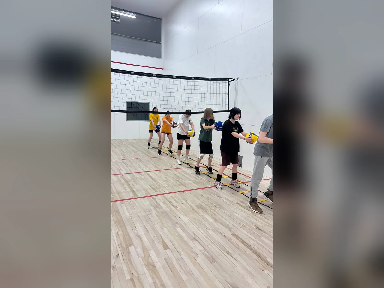 Юні волейболісти проходять вправу з координаційною драбиною, тримаючи м’ячі.